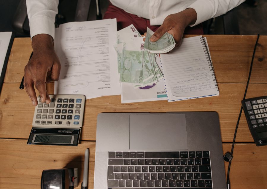 A person budgeting with a calculator, notebook and laptop